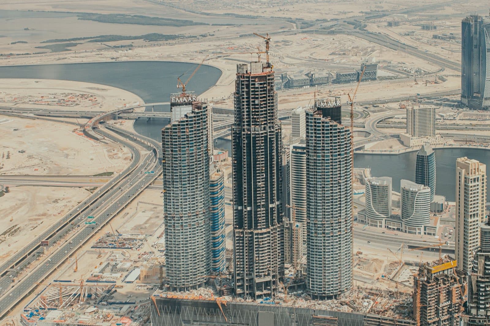 Emaar towers mid-construction in Dubai — bare cores and tower cranes amid roadworks